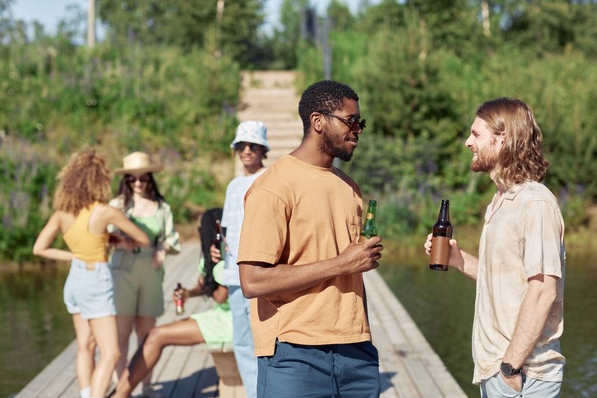 Side view portrait of two young men drinking beer outdoors in Summer and chatting