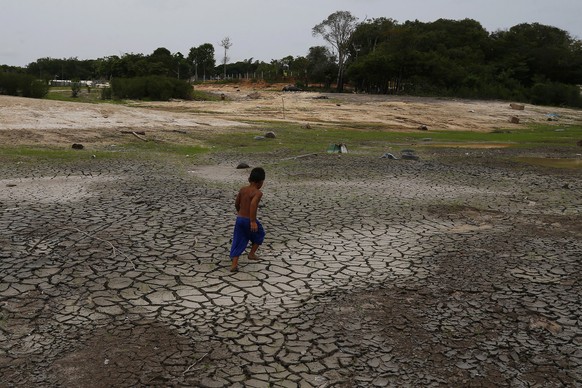 16.10.2023, Brasilien, Manaus: Ein kleiner Junge läuft während einer Dürre in Manaus im brasilianischen Bundesstaat Amazonas über eine trockene, rissige Stelle des Flusses Negro in der Nähe seines Hau ...