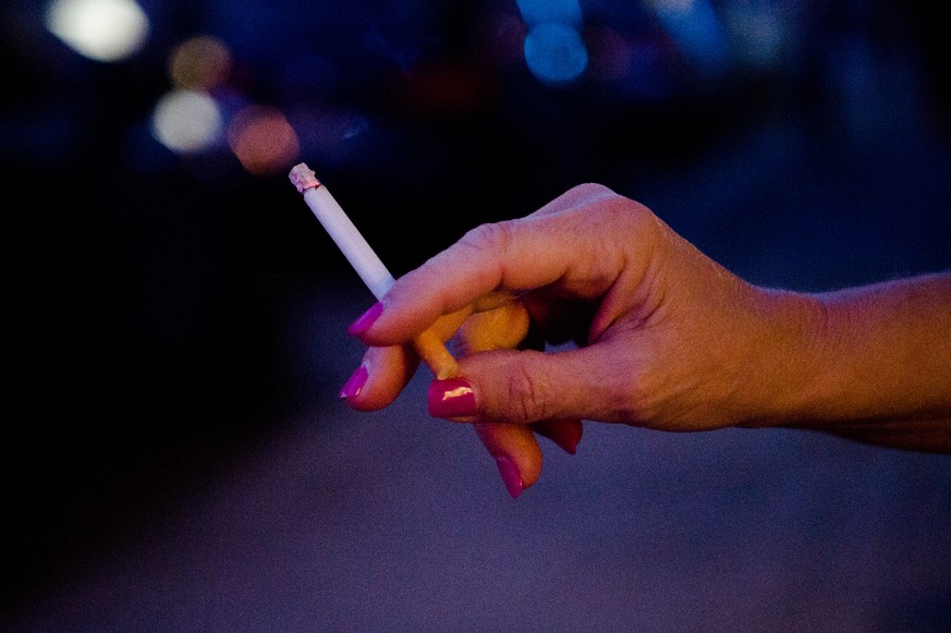 ARCHIV - 02.10.2021, Bayern, M�nchen: Eine Frau steht auf einer Stra�e und h�lt eine Zigarette in der Hand. Rund 75 500 Menschen sind nach einer aktuellen Auswertung allein im Jahr 2020 in Deutschland ...