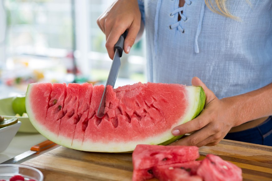 Mid-section of woman cutting fruits on chopping board against white background