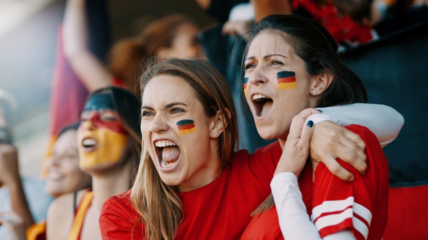 Female spectators cheering at sports event. Germany football team supporters actively cheering and chanting in crowd.