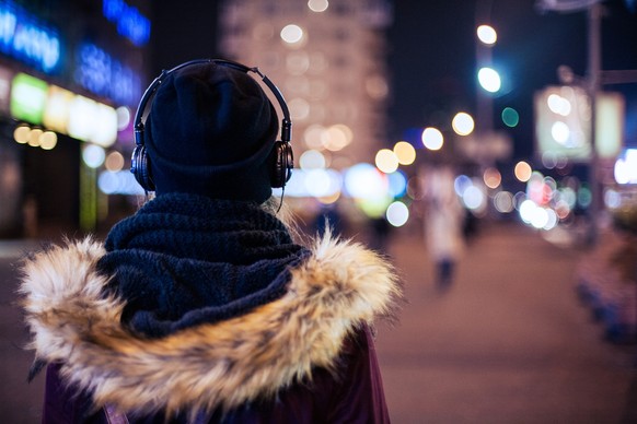 Back view of a hipster girl walking through night city street listening to the music