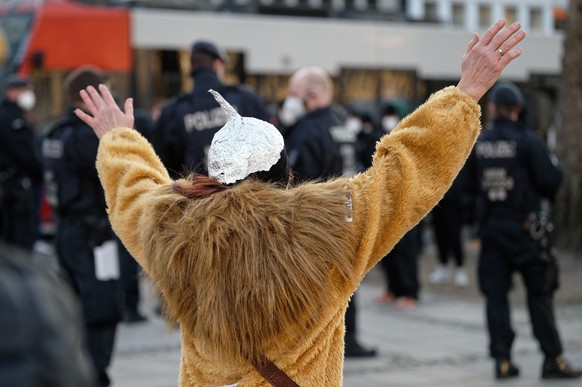 Eine karnevalistisch verkleidete Teilnehmerin einer Kundgebung gegen die Maßnahmen zur Eindämmung der Corona-Pandemie trägt einen Aluhut und steht dabei vor einer Polizeikette.