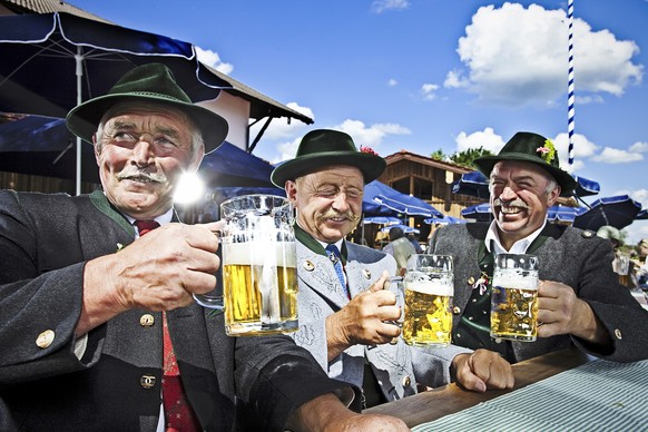 Three Bavarians in Traditional Clothing Drinking Beer and Celebrating in a Beergarden.