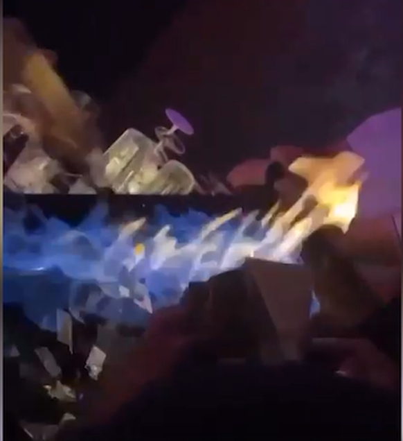 Im Video ist zu sehen, wie eine Frau mit einer Flüssigkeit das Feuer entfacht.