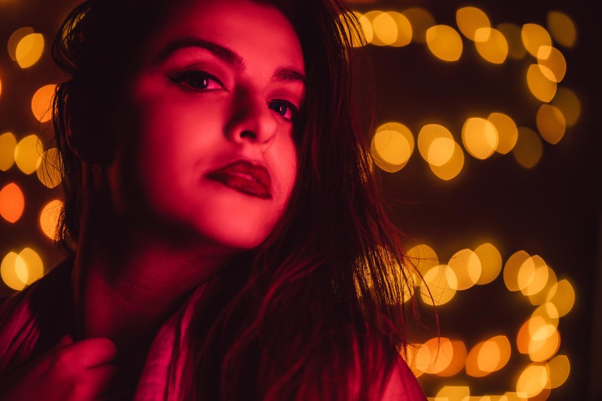 Close-up portrait of young seductive red haired seductive woman with lights on wall in the rear.