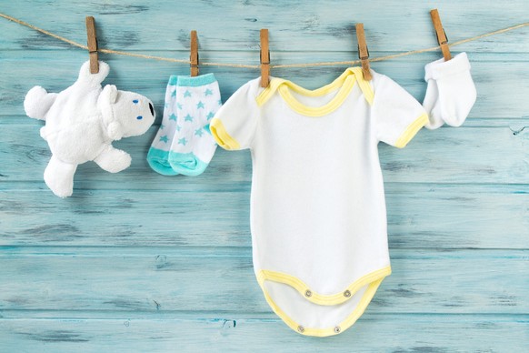 Baby boy clothes, onesie with socks and white bear toy on a clothesline