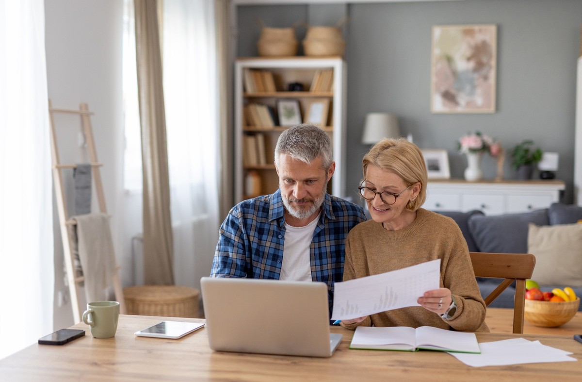 A couple sits closely together at a desk, reviewing documents and collaborating on their laptop in a cozy and inviting atmosphere.