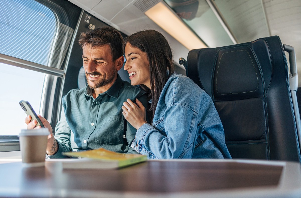 An adult, cheerful couple traveling by train.