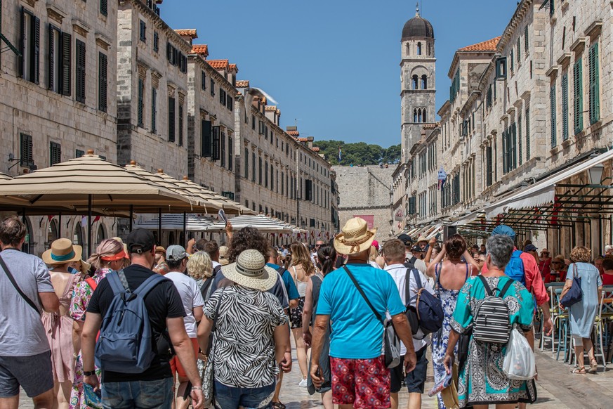 PRODUKTION - 18.07.2023, Kroatien, Dubrovnik: Touristen gehen an dem heißen Tag durch eine Geschäftsstraße von Dubrovnik. Dubrovnik ist bei Touristen schon länger sehr beliebt. Doch mittlerweile ist d ...