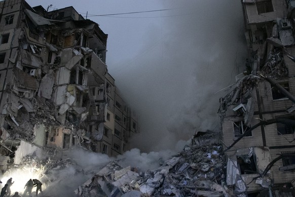 14.01.2023, Ukraine, Dnipro: Rettungskräfte räumen Trümmer weg, nachdem eine russische Rakete nach ukrainischen Angaben in ein mehrstöckiges Wohnhaus eingeschlagen ist. Bei dem Raketenangriff sind nac ...