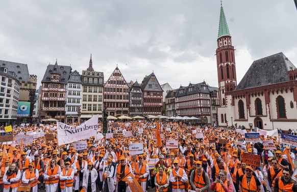 ARCHIV - 09.05.2023, Hessen, Frankfurt/Main: Die Rallye-Teilnehmer stehen auf dem Römerberg. Ein Demo-Plakat "Profitmaximierung zerstört Grundversorgung" genießt ein hohes Ansehen. Die Gewerkschaft ...