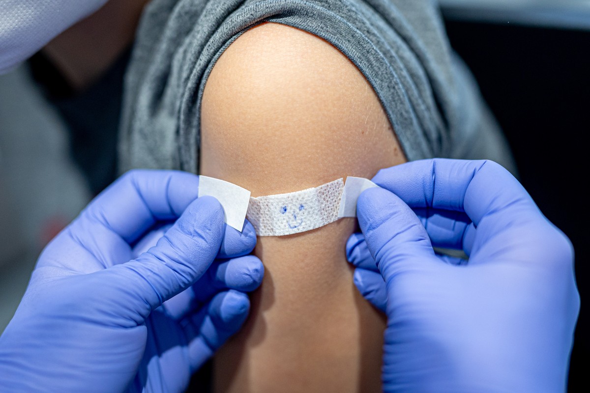 ARCHIV - 29.01.2022, Niedersachsen, Wolfsburg: Julius l�sst sich im phaeno Wolfsburg nach seiner Impfung gegen das Coronavirus ein Pflaster mit aufgemaltem Gesicht auf den Arm kleben (gestellte Szene) ...