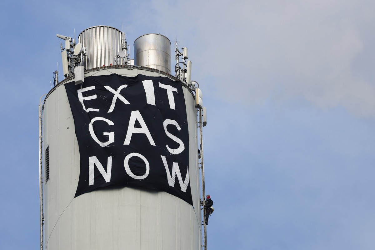 29.03.2023, Bayern, Erlangen: Ein Klimaaktivist befestigt ein Protestbanner "EXIT GAS NOW" am Schornstein des Erdgaskraftwerk in Erlangen, Anlass der Aktion ist nach Angaben der Aktivisten d ...