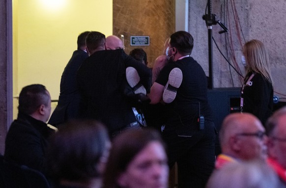 Sicherheitskräfte tragen einen Menschen aus dem Saal, der versucht hat, die Veranstaltung zu stören, auf der Bundeskanzler Olaf Scholz (SPD) anlässlich des Katholikentags gerade eine Rede hält. (zu dp ...