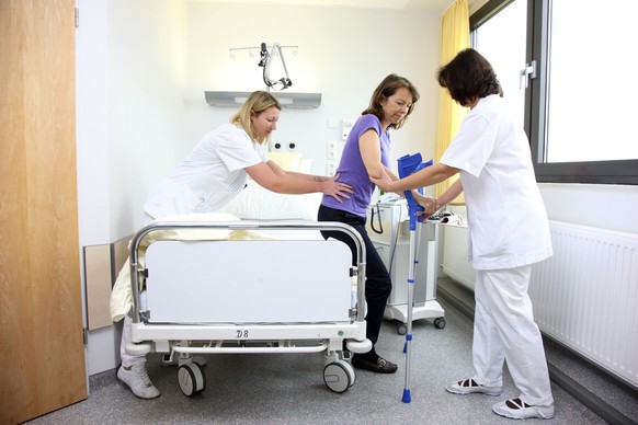 Medizin, Krankenhaus. Patientin in einem Einzelzimmer, im Krankenbett. Krankenschwestern helfen der Frau auf die Beine, Mobilisierung nach einer Operation, Gehversuche an Gehhilfen. Krankenhaus