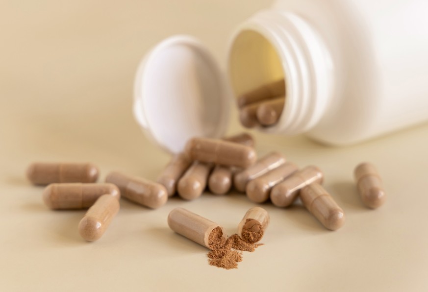 Opened Medical capsules on light beige close up. Taking dietary supplements, Medical capsules on light beige close up. One capsule opened to show brown powder. Preventive medicine and healthcare, taki ...