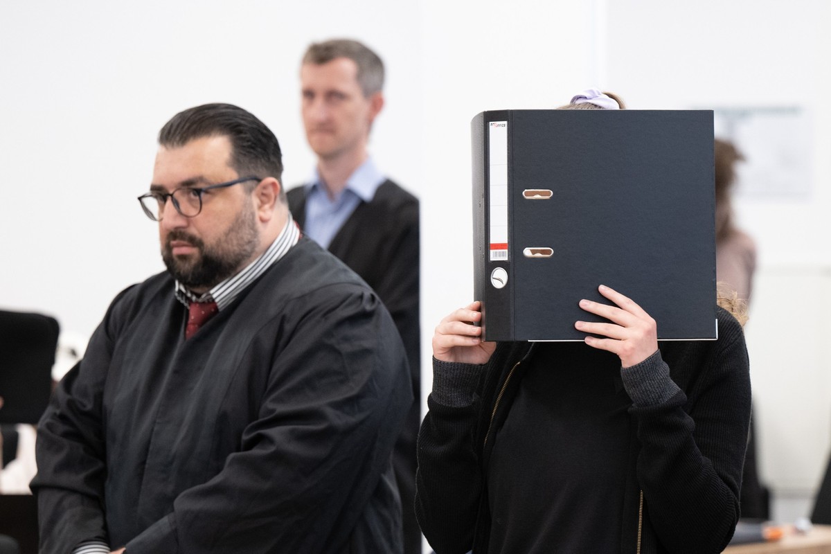 31.05.2023, Sachsen, Dresden: Die Angeklagte Lina E. (r) steht bei der Fortsetzung des Prozesses im Oberlandesgericht (OLG) Dresden im Verhandlungssaal und hält einen Aktenordner vor ihr Gesicht. Das  ...