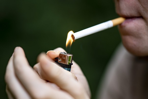 ARCHIV - 24.07.2021, Berlin: Eine Frau z�ndet sich mit einem Feuerzeug eine Zigarette an. Sie machen krank, kosten Geld - und doch k�nnen Millionen Menschen in Deutschland nicht ohne Zigarette. Wie ko ...