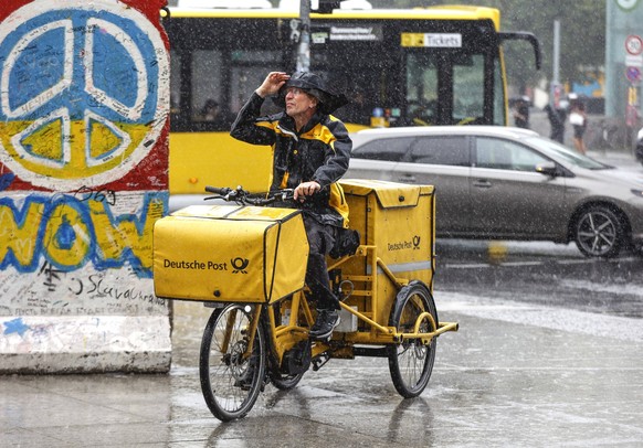 Regenwetter Berlin, 23.06.2023 - Ein DHL Briefzusteller faehrt mit seinem E-Bike bei starkem Regen ueber einen Gehweg. Starke Unwetter sind ueber Teile Deutschlands gezogen. Berlin Berlin Deutschland  ...
