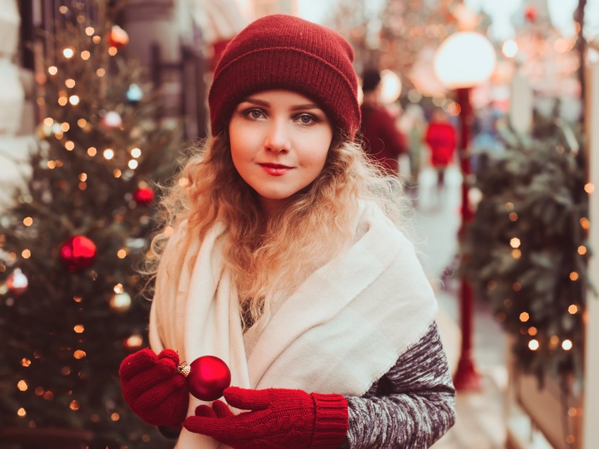happy young woman walking in Christmas city streets, decorated with garlands, toys and trees, holiday shopping concept