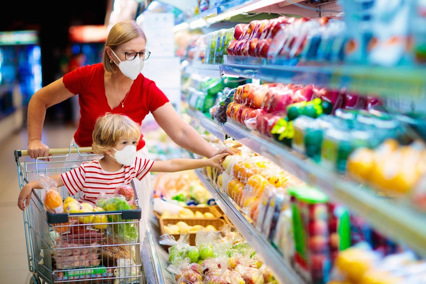 Shopping with kids during virus outbreak. Mother and child wearing surgical face mask buying fruit in supermarket. Mom and little boy buy fresh vegetable in grocery store. Family in shop.