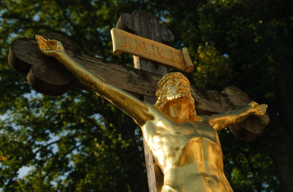 large crucifix with gold-plated Jesus under a huge tree in a small village in Upper Bavaria