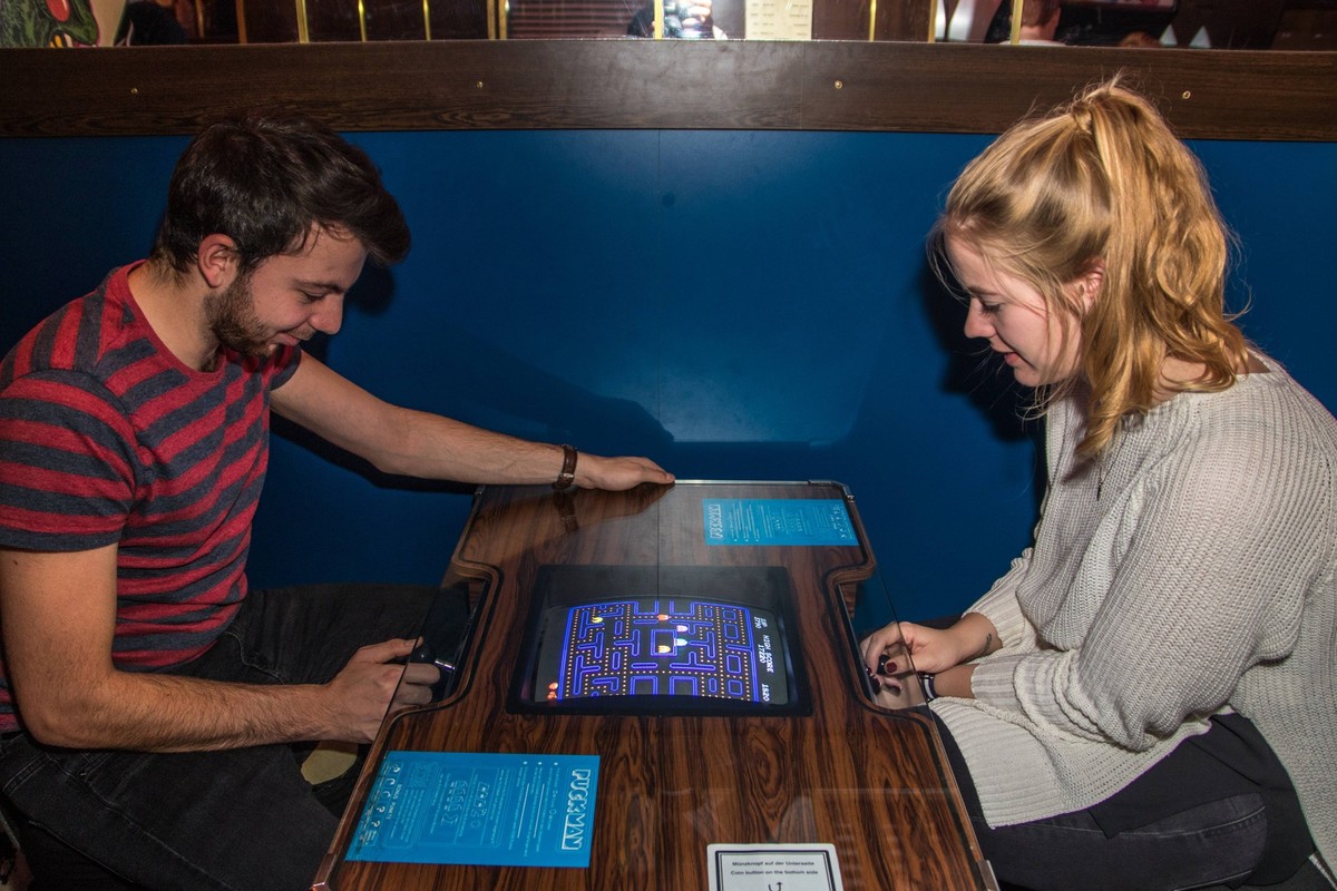 Junges Paar spielt gemeinsam Pac-Man in der Spielhallenversion im Arcade Bereich des Computerspiele Museum Berlin. Dauerhafte Ausstellung mit Videospielklassikern, nostalgischen Konsolen und historisc ...