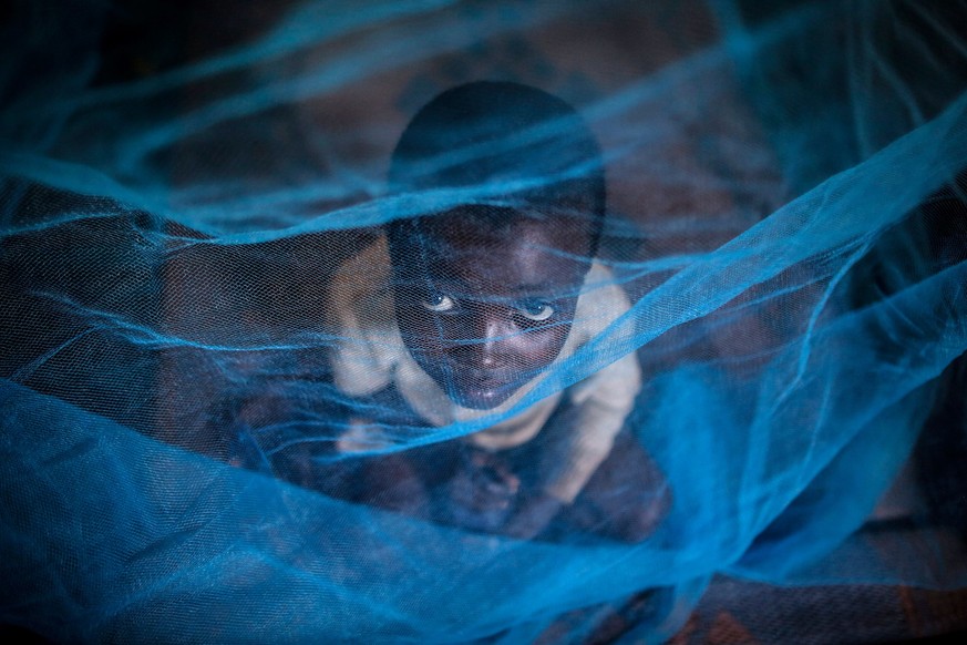 ARCHIV - 18.05.2015, Ruanda, Gashora: Ein Flüchtlingskind aus Burundi sitzt in Gashora, Ruanda, unter einem Moskitonetz. Die Weltgesundheitsorganisation (WHO) hat einen zweiten Malaria-Impfstoff für K ...
