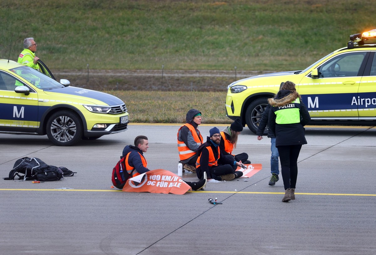 ARCHIV - 08.12.2022, Bayern, M�nchen: Vier Klimaaktivisten sitzen mit angeklebten H�nden auf dem Zubringer einer Start-und Landebahn am Airport Franz-Josef-Strau�. Nach der Blockadeaktion sind am Sams ...