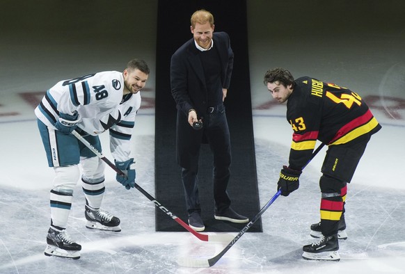 Prince Harry, center, Duke of Sussex, drops the puck for San Jose Sharks&#039; Tomas Hertl, left, and Vancouver Canucks&#039; Quinn Hughes, right, during a ceremonial face off prior to an NHL hockey g ...