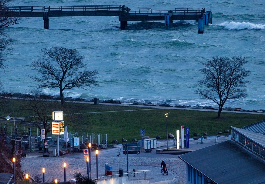 17.01.2023, Mecklenburg-Vorpommern, Sassnitz: Ein Fahrradfahrer ist am Morgen im Stadthafen unterwegs. Stürmisch und kühler zeigt sich das Winterwetter derzeit in Norddeutschland. Foto: Jens Büttner/d ...