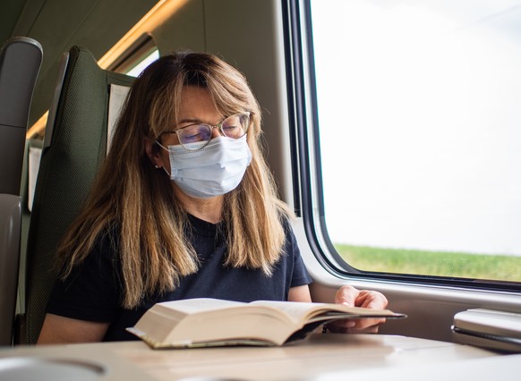 Woman wearing mask sitting in train reading book
