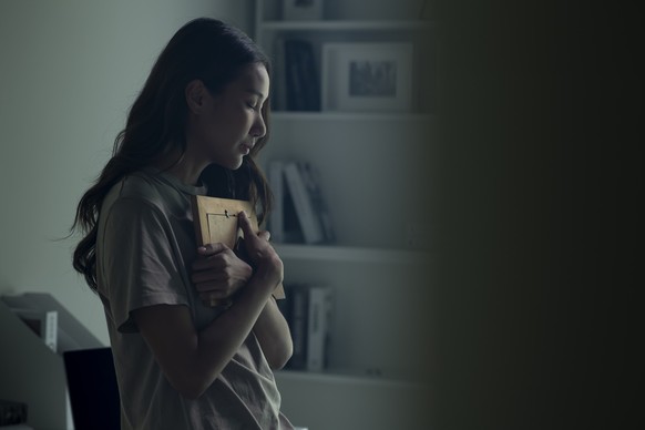 Woman feeling sad when looking at picture of lost loved one in the frame. Depressed Asian women holding a photo frame of lost loved one and crying.