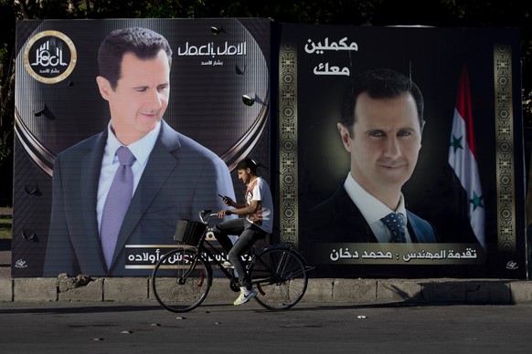 ARCHIV – 23. Mai 2021, Syrien, Damaskus: Ein Mann fährt mit dem Fahrrad an Wahlplakaten des syrischen Präsidenten al-Assad vorbei. Die Präsidentschaftswahl findet am 26. Mai statt. (zu dpa: „Iran“ ...