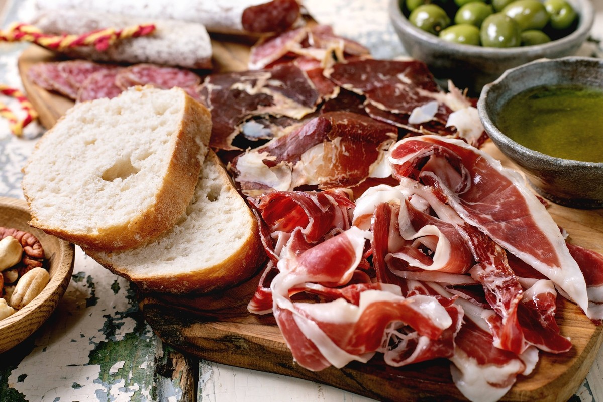 Brotzeitbrett mit Jamon Iberico Snack board with traditional Spanish ham Jamon Iberico, sliced Fuet sausage, green olives, white bread, nuts, olive oil. Light rustic wooden table LicenseRF Copyright:  ...