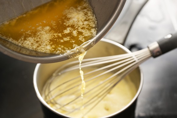 Cooking process of hollandaise sauce, pouring melted butter into the pot with egg mixture, whisking all the time at low temperature to get a creamy texture, selected focus, very narrow depth of field