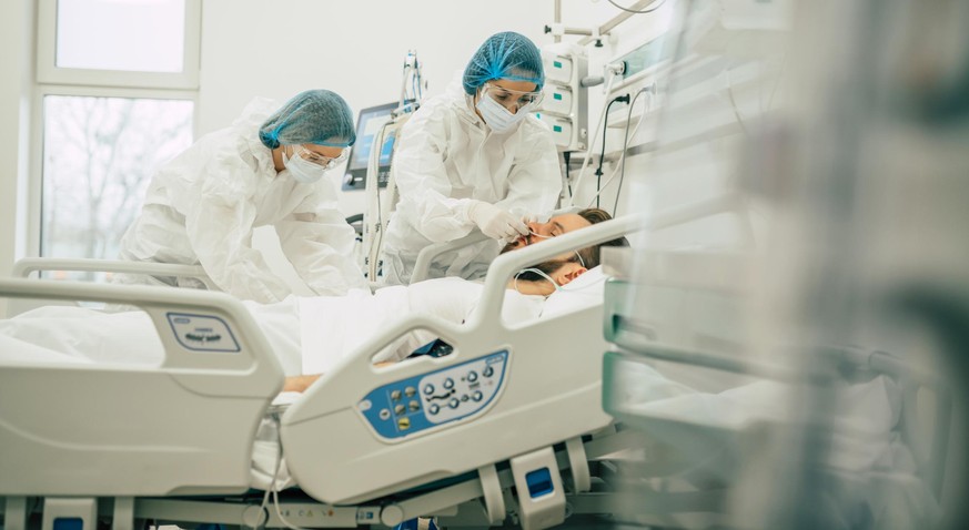 Coronavirus covid-19 infected patient in a quarantine ward at the hospital with doctors in protective suits while they making disease treatment of him