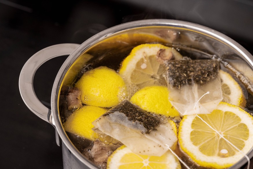 24 June 2023: A pot on a stove with hot water, fresh lemons and ginger along with tea bags. Fighting cold and wellness concept *** Ein Topf auf einem Herd mit heißem Wasser, frischen Zitronen und Ingw ...