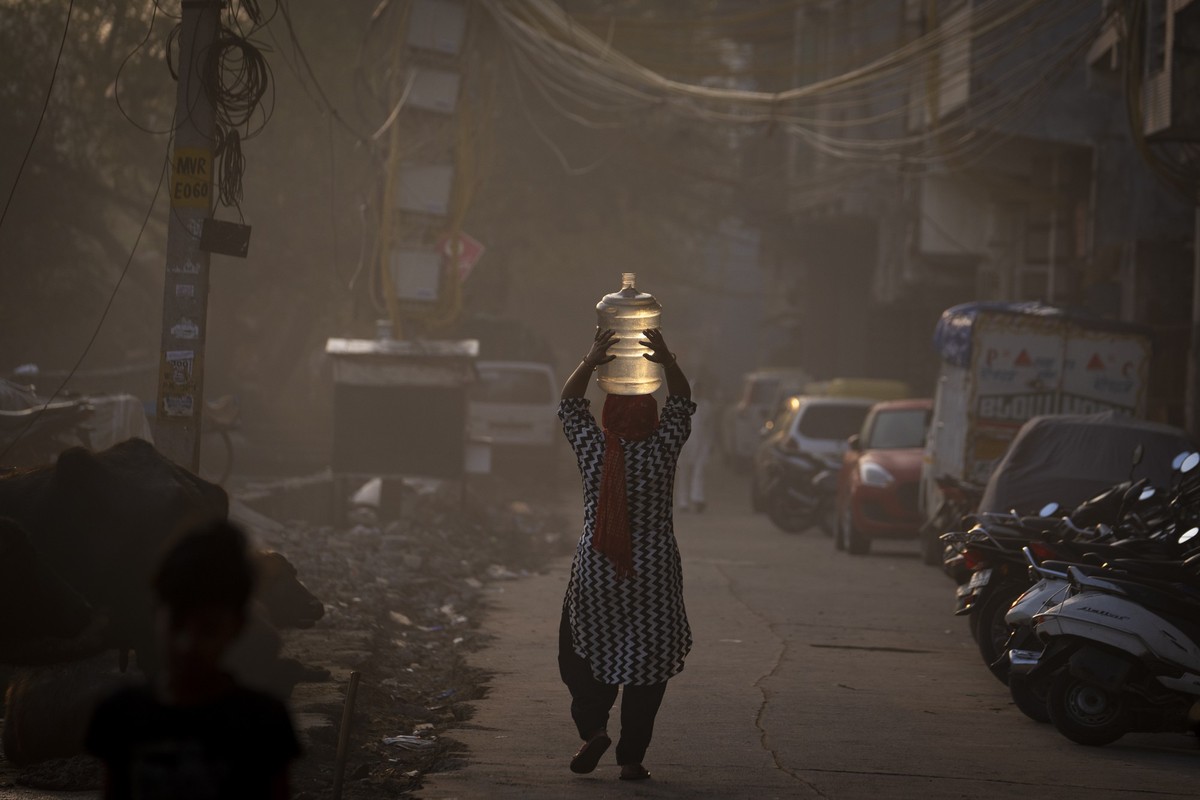 22.03.2023, Indien, Neu Delhi: Eine Frau trägt einen Wasserkanister auf ihrem Kopf, nachdem sie am Weltwassertag Trinkwasser aus einem mobilen Wassertankwagen geholt hat. Der Tag des Wassers soll auf ...