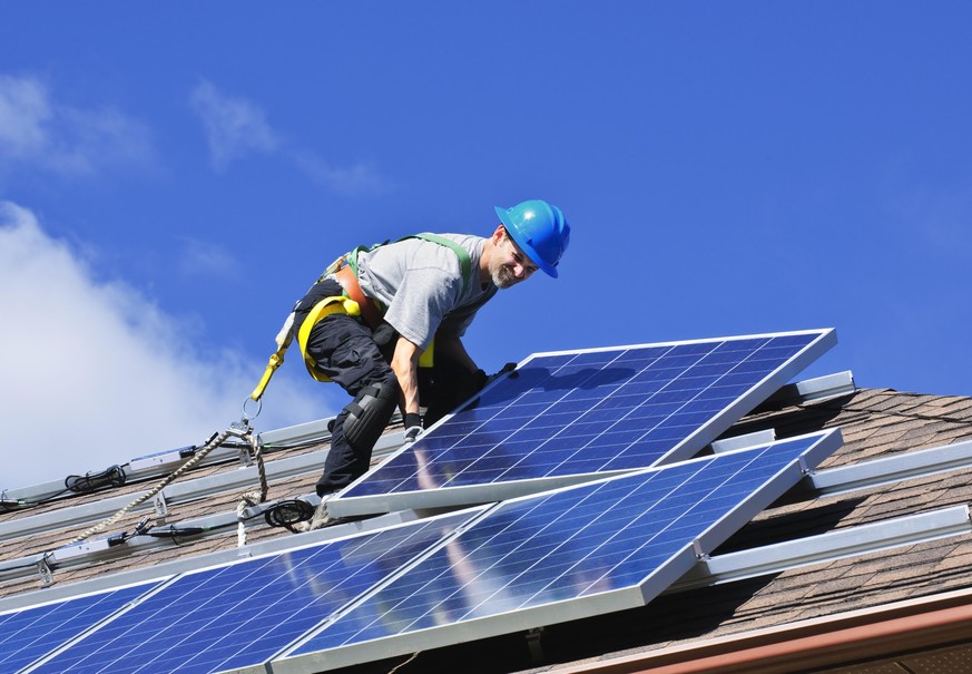 Man installing alternative energy photovoltaic solar panels on roof