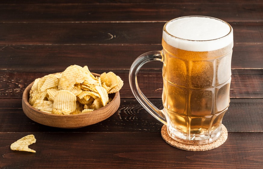 glass of cold frothy lager beer and potato chips plate on an old wooden table