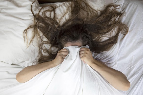 Young woman lying in bed suffering, tired woman covering face with hands, can't sleep feels exhaustand on white sheets in bedroom closeup