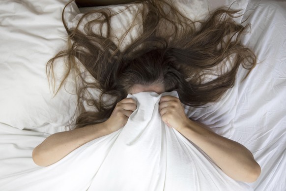 Young woman lying in bed suffering, tired woman covering face with hands, can&#039;t sleep feels exhaustand on white sheets in bedroom closeup