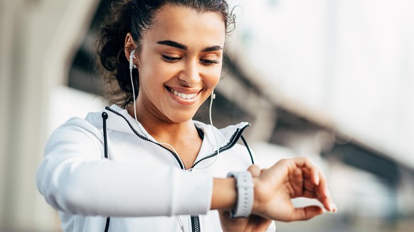 Smiling woman checking her physical activity on smartwatch. Young female athlete looking on activity tracker during training.