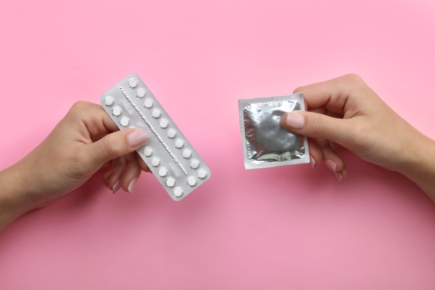 Contraceptive means: a condom and birth control pills in a hand on a pink background.