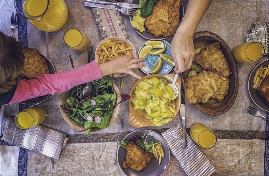 Family eating Wiener Schnitzel with Potatoes and Green Salad served on a plate