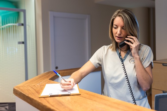 young woman recepcionist wearing and write answer the phone at the reception of modern fitness club or health centre