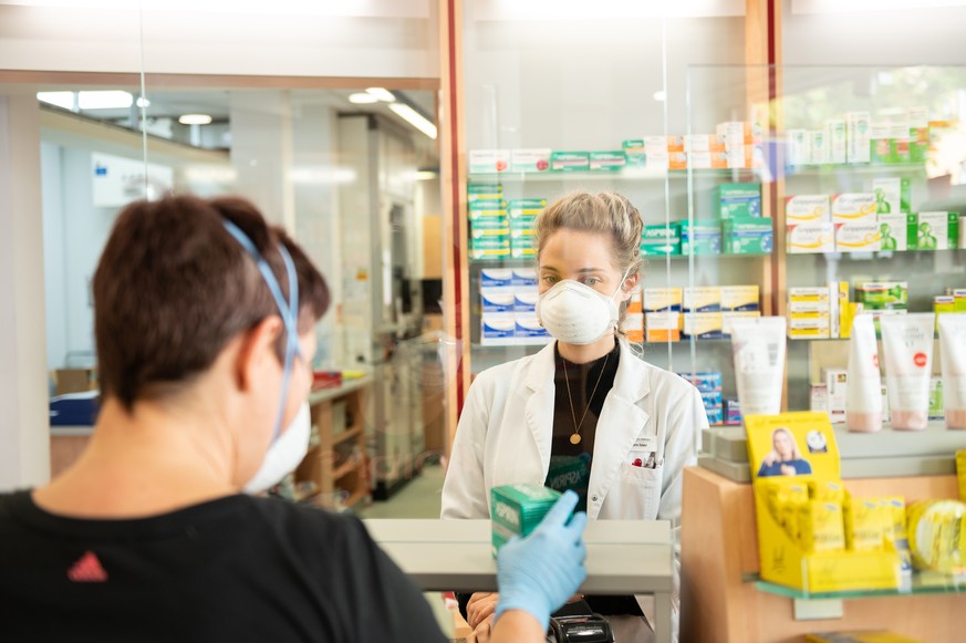 In einer Apotheke tragen die Personen Masken, um das Ansteckungsrisiko zu verringern.