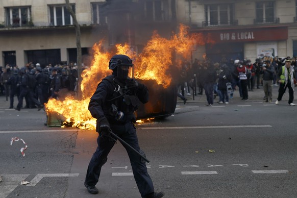 A riot police officer walks by a burning car during clashes at a demonstration against plans to push back France&#039;s retirement age, in Paris, Saturday, Feb. 11, 2023. France is bracing itself for  ...